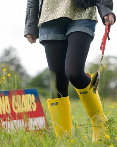 Yellow coloured Cotswold Sandringham Buckle Strap Wellingtons on grassy background #colour_yellow