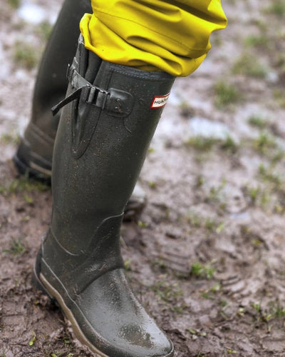 Dark Olive coloured Hunter Mens Balmoral Neoprene Adjustable Wellington Boots on mud background #colour_dark-olive