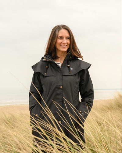 Black Lighthouse Outback Full Length Ladies Waterproof Raincoat on beach background #colour_black