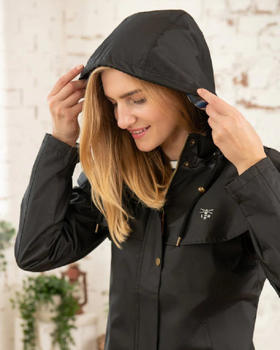 Black coloured Lighthouse Outrider 3/4 Length Ladies Waterproof Raincoat on wall background #colour_black