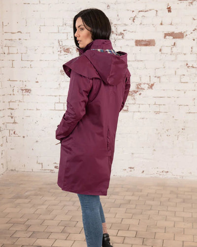 Plum coloured Lighthouse Outrider 3/4 Length Ladies Waterproof Raincoat on wall background #colour_plum