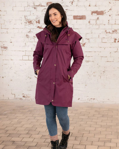 Plum coloured Lighthouse Outrider 3/4 Length Ladies Waterproof Raincoat on wall background #colour_plum